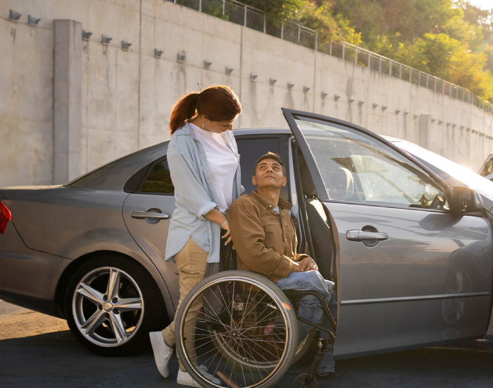 A woman assisting a man in a wheelchair into a car, highlighting NDIS Transport Support Services